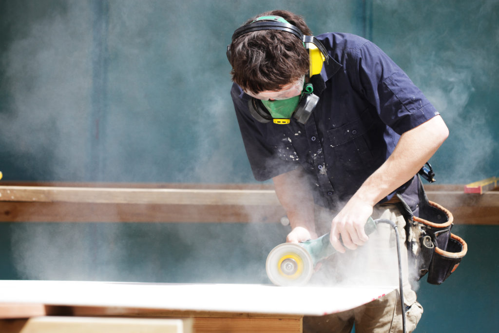 Apprentice using angle grinder to cut cement sheet